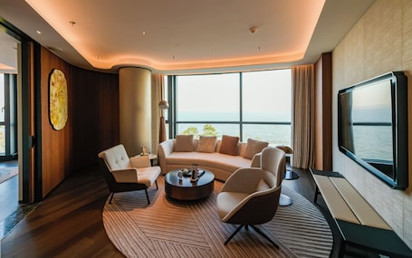 A modern living room with a curved sofa, a coffee table, and a large window with a view of the sea.