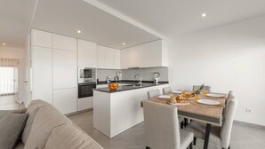 Una cocina moderna con armarios blancos, una isla central y un comedor con mesa de madera y sillas grises.