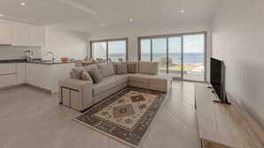 Una sala de estar moderna con un sofá seccional color beige, un televisor de pantalla plana y un ventanal con vistas al mar.