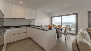 Una cocina moderna con armarios blancos, encimera negra y un amplio ventanal con vistas al mar.
