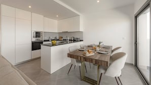 Une cuisine moderne avec des meubles blancs, un îlot central et un coin repas comprenant une table en bois et des chaises blanches.