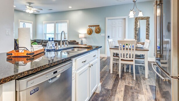 A modern kitchen with granite countertops, stainless steel appliances, and a dining area with a wooden table and chairs. - Good Gulf Times · New Listing! Heated Pool, Hot Tub & Steps to Beach (Gulf Shores)