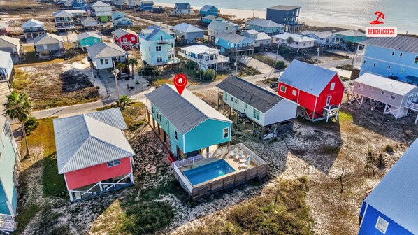 Vista aérea de uma área residencial costeira com casas, uma piscina e uma praia ao fundo.