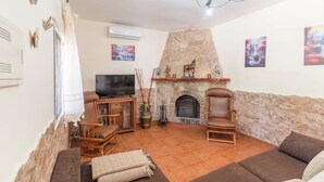 Un salon avec une cheminée en pierre, un téléviseur et deux fauteuils en bois.