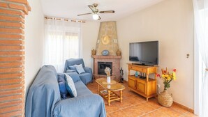 A living room with a brick fireplace, a television on a wooden stand, a blue sofa, and a coffee table. - El Ranchito Torrox by Ruralidays (Málaga)