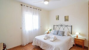 A neatly made bed with a white bedspread and pillows, a bedside table with a lamp, and a window with sheer curtains. - El Ranchito Torrox by Ruralidays (Málaga)