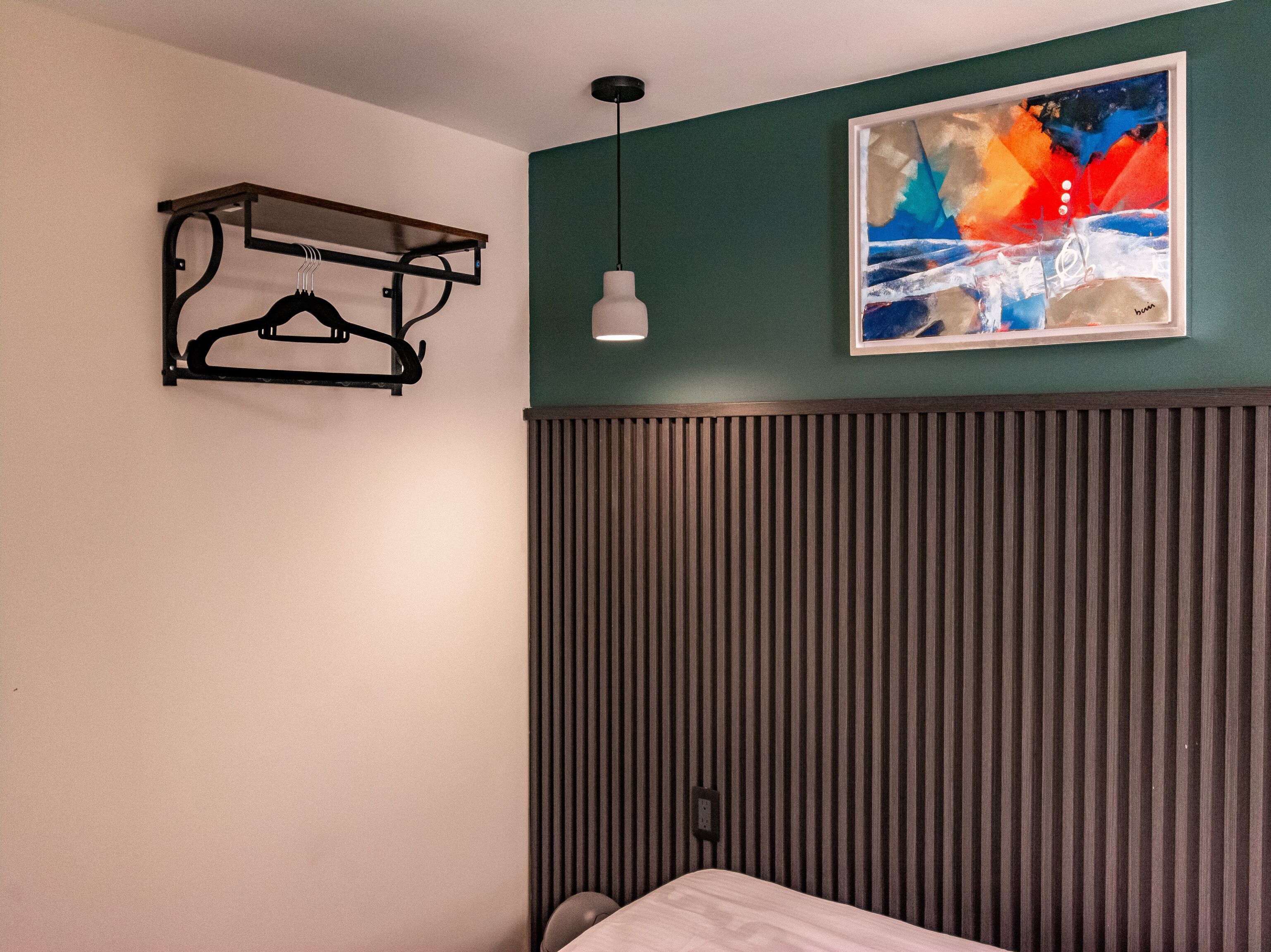 Une chambre d’hôtel avec un lit, un luminaire fixé au mur, un tableau et un radiateur.