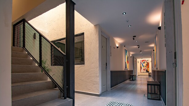 Un couloir d’hôtel moderne avec un sol à motifs géométriques, un escalier doté d’une rampe en métal et un éclairage encastré.