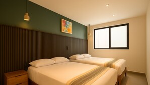 Une chambre d’hôtel avec deux lits, une table de chevet en bois, une petite table, une fenêtre avec des stores et un tableau au mur.