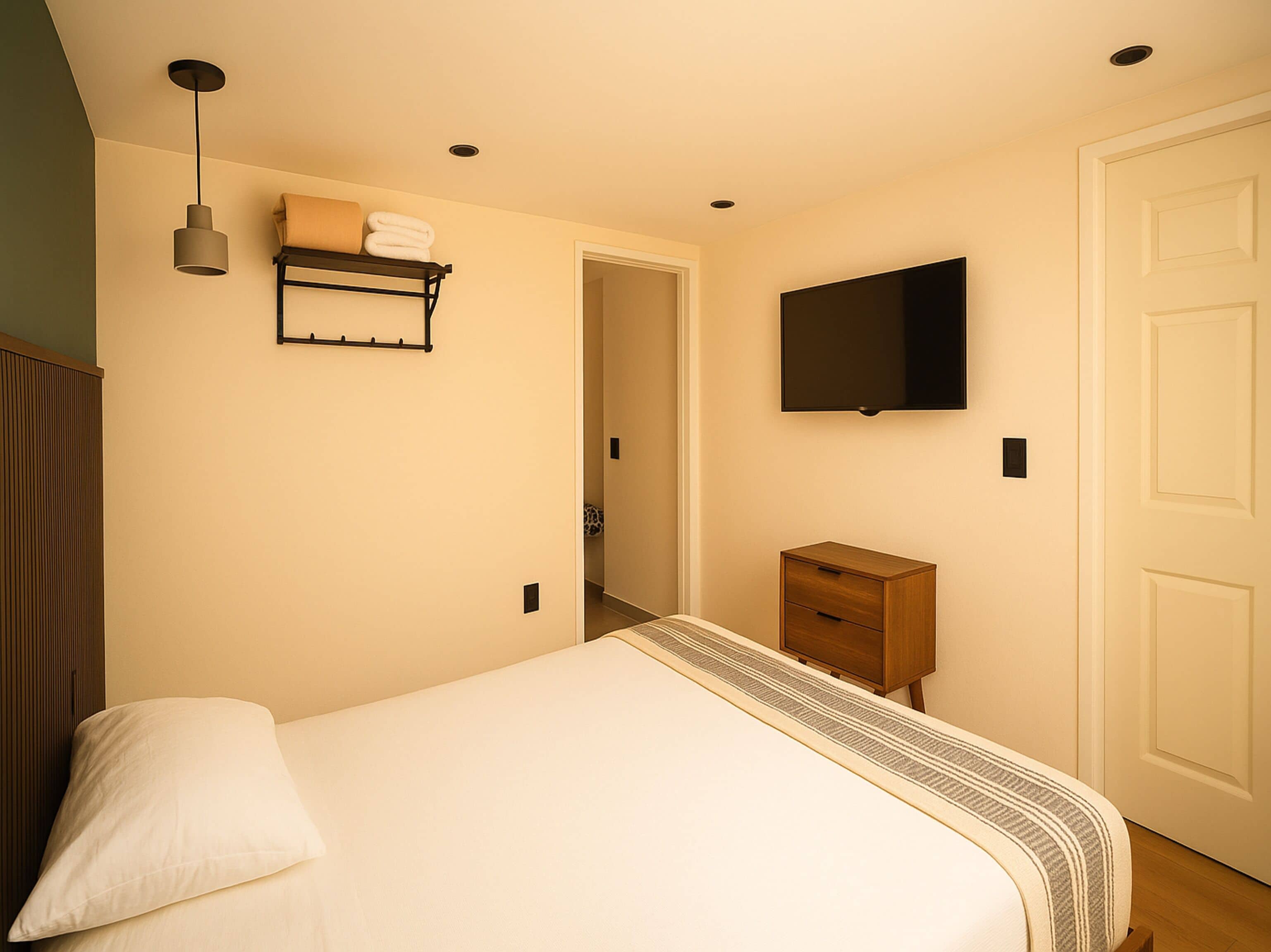 A bedroom with a bed, a bedside table, a TV mounted on the wall, and a door.