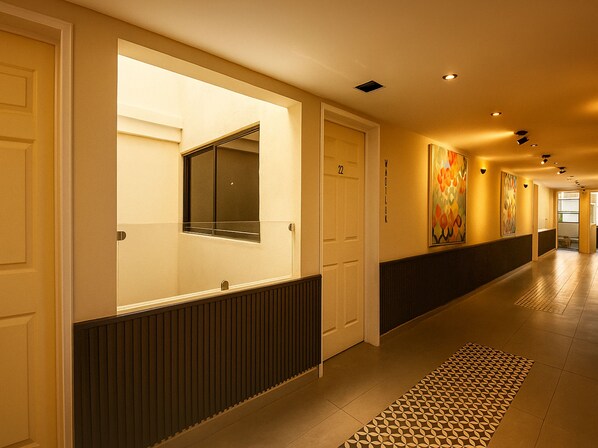 Un pasillo de hotel con diseño moderno, que presenta un largo corredor, puertas y un suelo estampado.