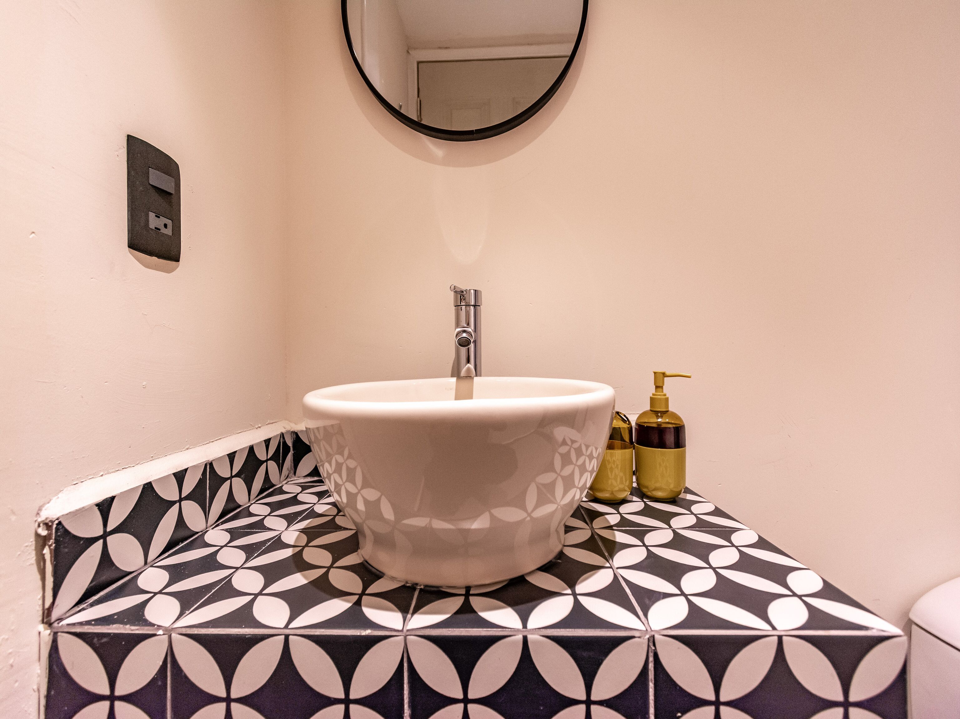 Une salle de bain avec un lavabo blanc, un miroir au-dessus, et des carreaux à motifs sur le sol et les murs.