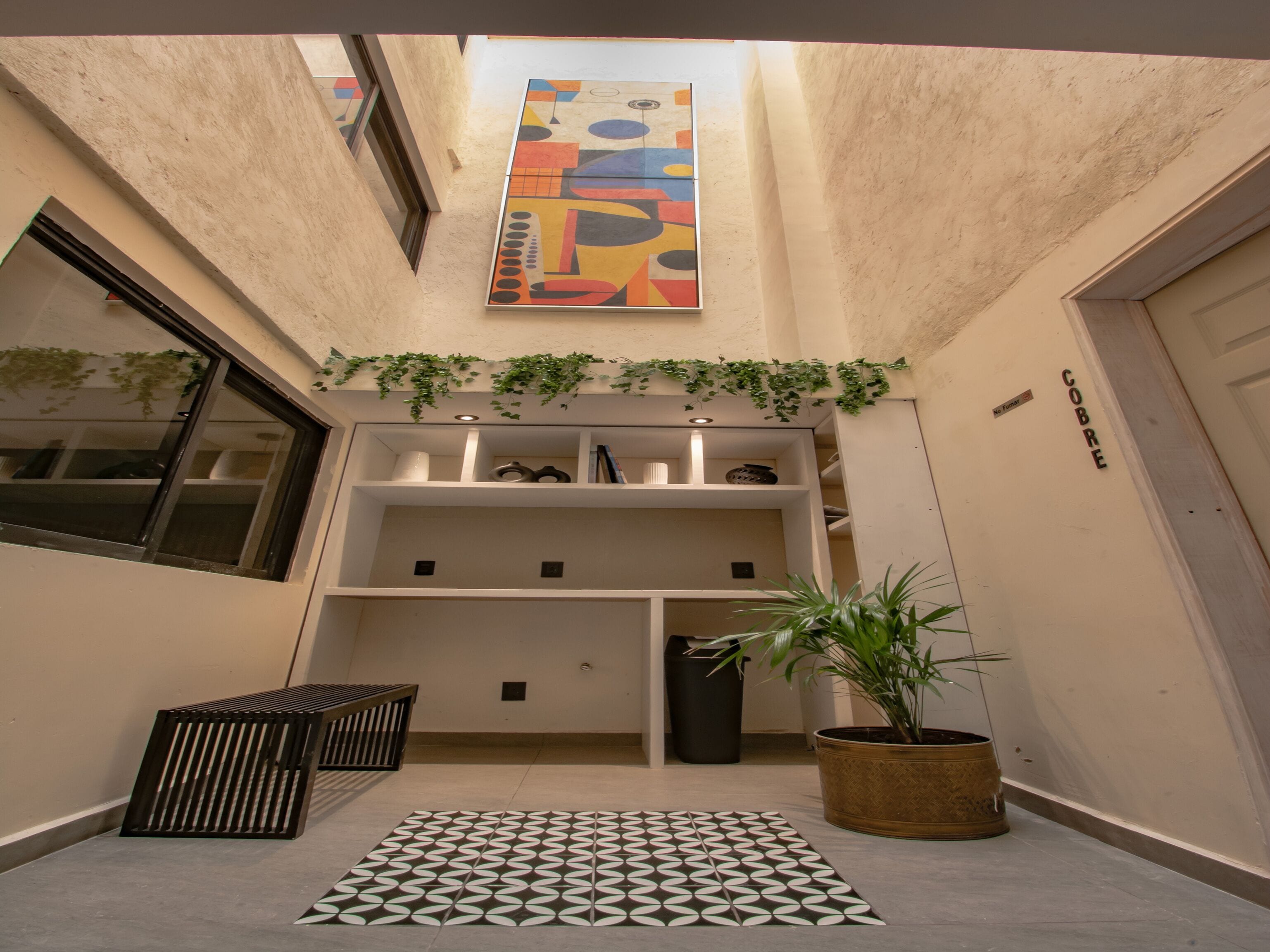 Un couloir étroit avec un sol à motifs, une plante en pot et un tableau abstrait aux couleurs vives accroché au mur.