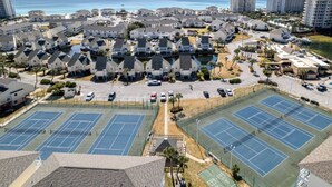 Et boligområde med flere tennisbaner, en parkeringsplads og udsigt til havet.