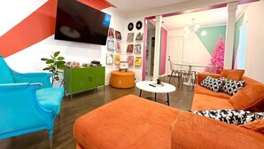 A living room with a sofa, a chair, a small table, a green cabinet, and a TV mounted on the wall. - Retro Style / Walk to Rangers / AT&T Stadium / Hot Tub (Arlington)
