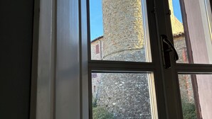 A window with a view of a stone tower and a stone wall. - Guest House Foschi - Cozy Home in a Medieval Village (Castiglion Fosco)