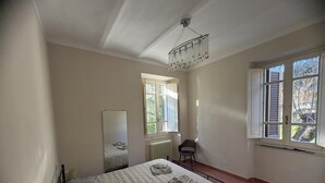 A bedroom with a bed, a chair, a mirror, and a window with shutters. - Guest House Foschi - Cozy Home in a Medieval Village (Castiglion Fosco)