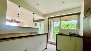 Een moderne keuken met een groot kookeiland, inbouwvoorraden en een raam met uitzicht op groen.