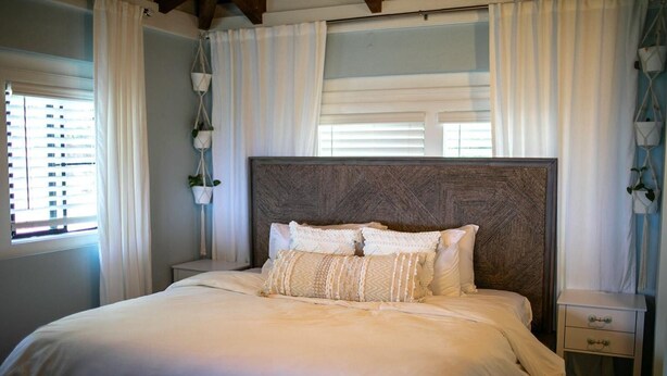 Uma cama bem arrumada com várias almofadas, uma cabeceira de madeira e uma mesa de cabeceira com uma gaveta.