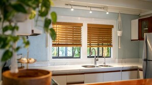 Cozinha com persianas de madeira, pia de aço inoxidável e luminária pendente.