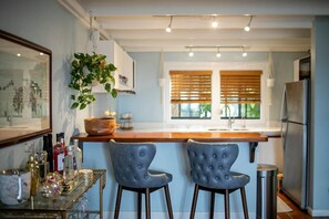 A modern kitchen with a bar area, two tufted chairs, a hanging plant, and a stainless steel refrigerator. - Cruz Bay 1BR Loft, Pool, A/C, Backup Power + In-House Car Rental (Cruz Bay)