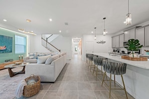 A modern kitchen with a bar area, a staircase leading to another level, and a living room with a sofa and a coffee table. - New Welcoming Resort Home w/ Private Pool, sleeps 20 (Kissimmee)