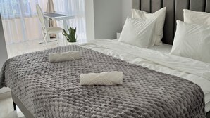 A modern bedroom with a large bed, grey and white bedding, a grey headboard, and a view of a balcony with a chair and plant. - Luxury Villa with Private Pool in a Quiet Setting (Mazarrón)