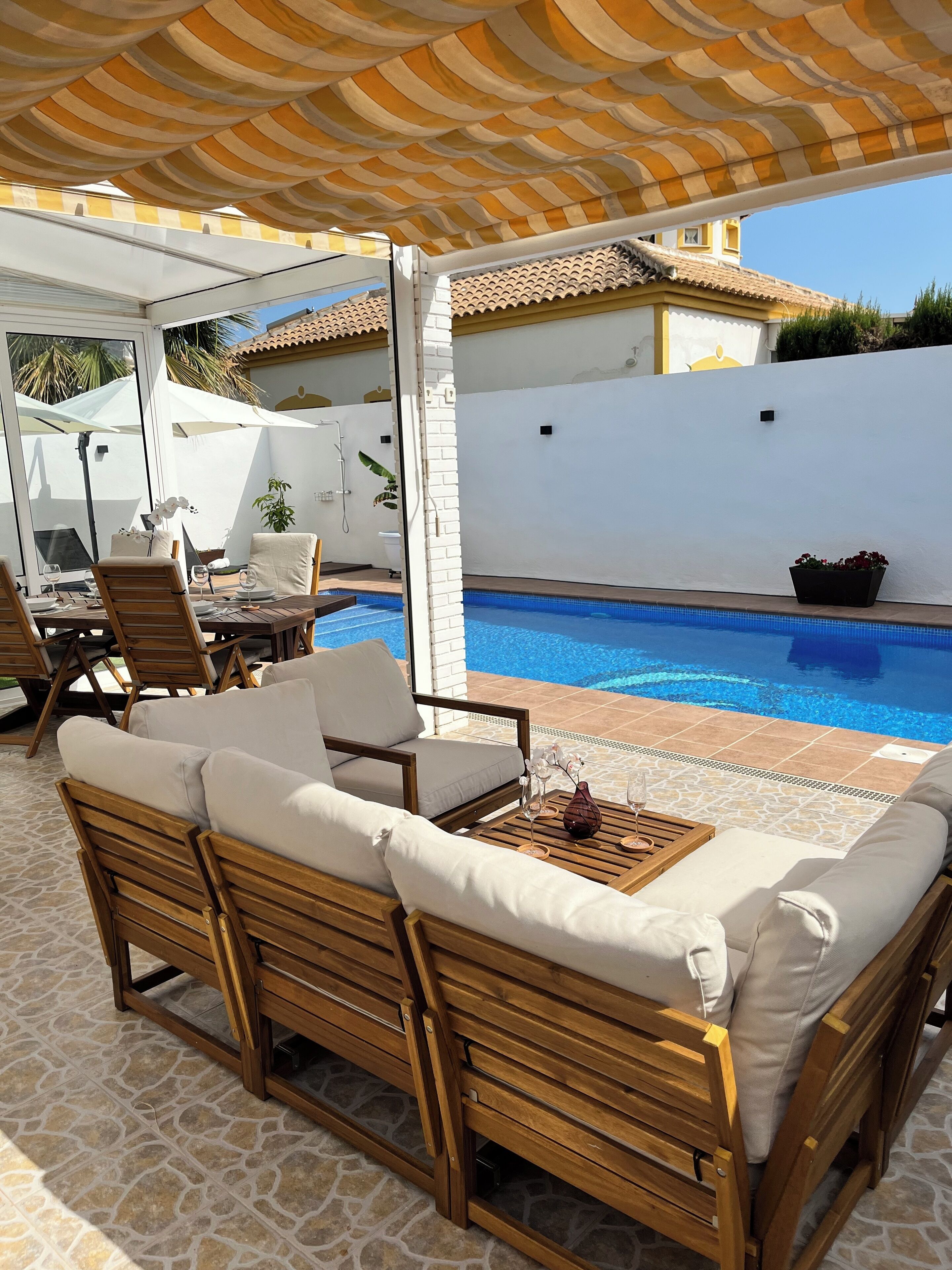 Un espace aménagé au bord de la piscine, avec des chaises longues en bois et un coin salon abrité.