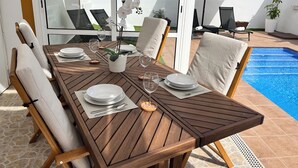 A wooden dining table set with white plates, silverware, and wine glasses, surrounded by cushioned chairs. - Luxury Villa with Private Pool in a Quiet Setting (Mazarrón)