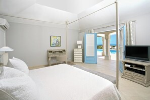 Ein Hotelzimmer mit einem großen Bett, einem Fernseher, einem Schreibtisch und Blick auf den Pool.