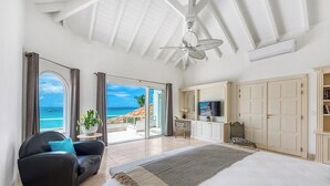 Ein geräumiges Schlafzimmer mit einem großen Bett, einem Deckenventilator, einem Fernseher und Blick aufs Meer.