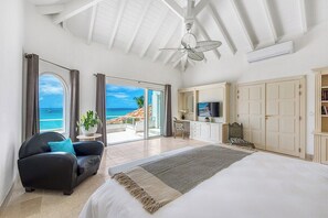 Ein geräumiges Schlafzimmer mit einem großen Bett, einem Deckenventilator, einem Fernseher und Blick aufs Meer.