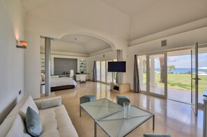 A modern hotel room with a large bed, a TV, a glass table, and a view of the ocean. - Sandyline   Private Paradise   Resort Style Villa (Saint Martin)