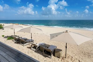 Ein Strand mit Liegestühlen und Sonnenschirmen, ein Holzdeck und das Meer im Hintergrund.
