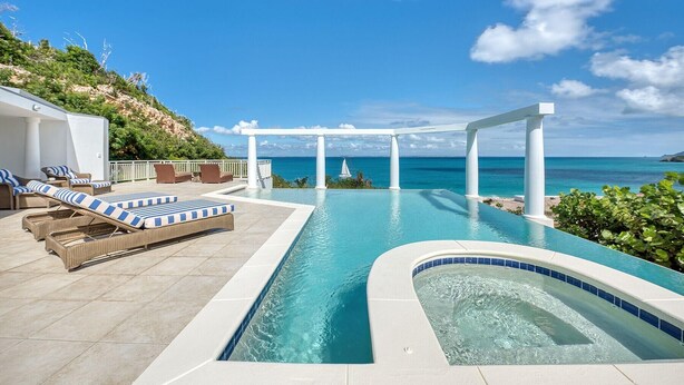 Un área de piscina con sillones de descanso, un jacuzzi y vistas al océano.