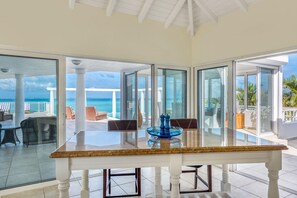 Ein geräumiges Zimmer mit einem großen Glastisch und Stühlen, Meerblick und einem Balkon mit Sitzgelegenheit.