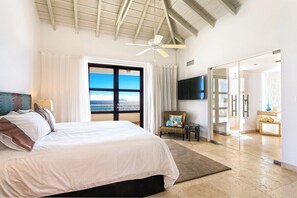 A spacious bedroom with a large bed, a ceiling fan, a view of the ocean through a sliding glass door, and a TV mounted on the wall. - Farniente   Shore Pointe villa with Ocean Views (Saint Martin)