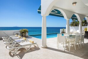 A poolside area with lounge chairs and a table, overlooking a clear blue sea. - Farniente   Shore Pointe villa with Ocean Views (Saint Martin)