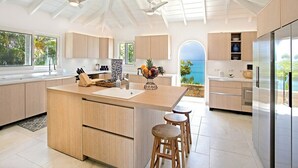 A modern kitchen with a central island, wooden bar stools, and a view of the ocean. - Libellule   Elevated Beachfront Villa (Saint Martin)
