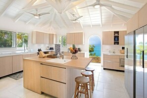 A modern kitchen with a central island, wooden bar stools, and a view of the ocean. - Libellule   Elevated Beachfront Villa (Saint Martin)