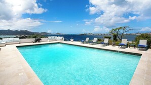 A rectangular swimming pool with clear blue water, surrounded by lounge chairs and a view of the sea and mountains. - Libellule   Elevated Beachfront Villa (Saint Martin)