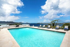 A rectangular swimming pool with clear blue water, surrounded by lounge chairs and a view of the sea and mountains. - Libellule   Elevated Beachfront Villa (Saint Martin)