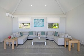 A modern living room with a grey sectional sofa, two wooden side tables, a central coffee table, and a large abstract painting on the wall. - Ocean View   Stunning Orient Bay Villa (Saint Martin)