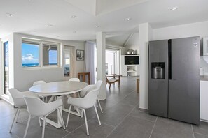 A modern kitchen with a stainless steel refrigerator, a dining area with white chairs, and large windows offering a view of the sea. - Ocean View   Stunning Orient Bay Villa (Saint Martin)