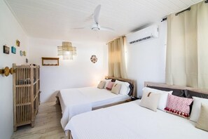 A bedroom with two beds, a ceiling fan, a wooden wardrobe, and a wall-mounted air conditioner. - Mary's Beach Cottage: Seashore (Saint Martin)