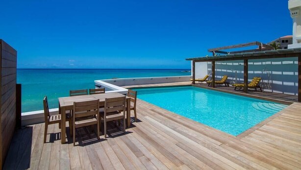 A wooden deck with a pool and lounge chairs overlooking a clear blue sea. - Mary's Beach Cottage: Seashore (Saint Martin)