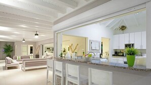 A modern kitchen with white cabinets, a large island with bar stools, and a view into the living area with a sofa and chairs. - Giselle   Stunning ocean views (Saint Martin)