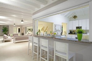 Eine moderne Küche mit weißen Schränken, einer großen Kochinsel mit Barhocker und Blick in den Wohnbereich mit Sofa und Sesseln.