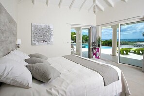 Ein modernes Schlafzimmer mit einem großen Bett, Blick auf den Pool und Sitzgelegenheiten im Freien sowie einem großen Fenster.