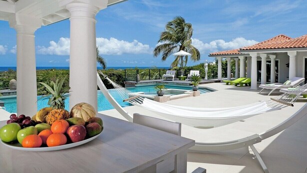 A poolside area with a view of the ocean, a dining table with fruit, and lounge chairs. - Giselle   Stunning ocean views (Saint Martin)